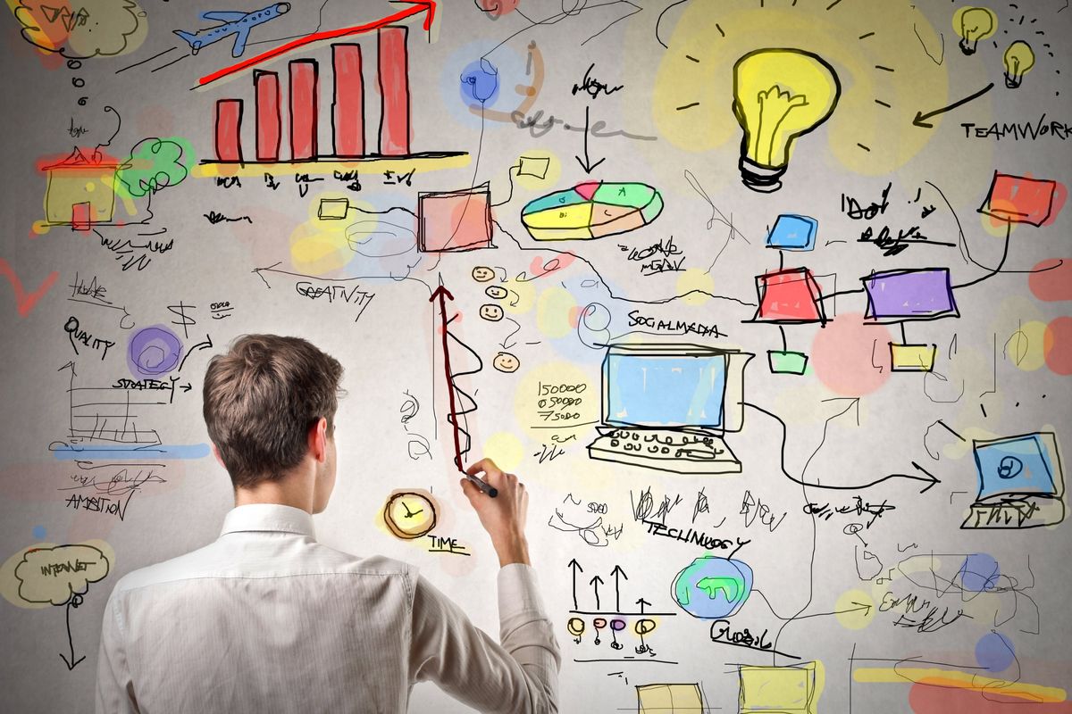 Marketer sketching a marketing plan on a whiteboard with charts, social media and website drawings