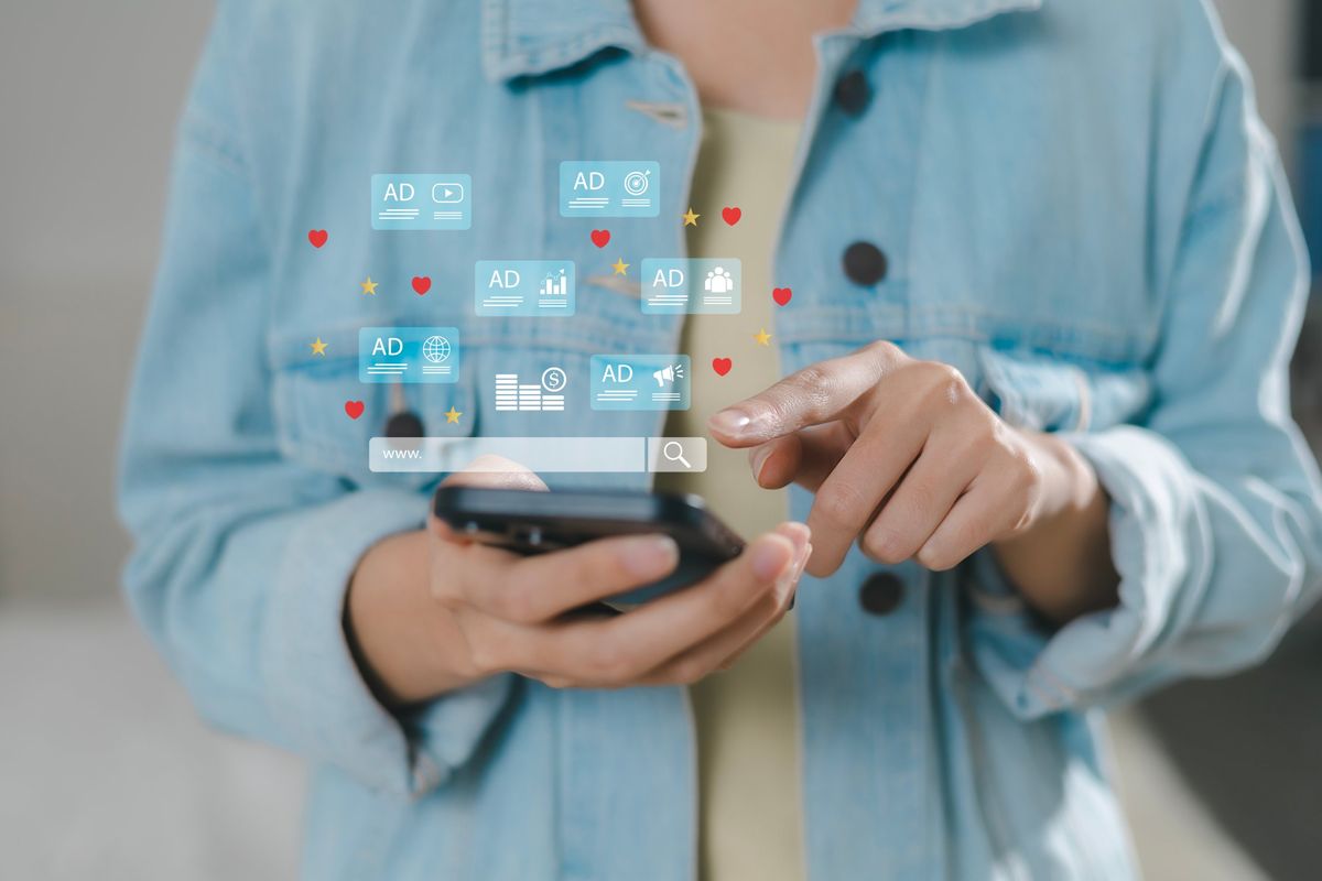 Person holding a smartphone with ad icons and a search bar shown above the screen