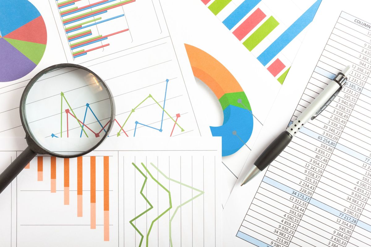 Magnifying glass over printed line charts, bar charts and a spreadsheet of website traffic data
